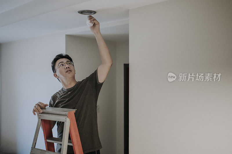 an asian chinese mid adult male changing light bulb in living room, apartment home